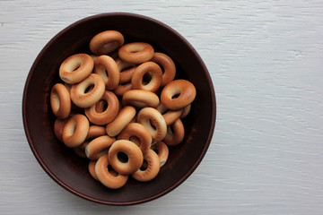 Small dry bagels for kids in brown ceramic bowl on white wooden background. Healthy snack