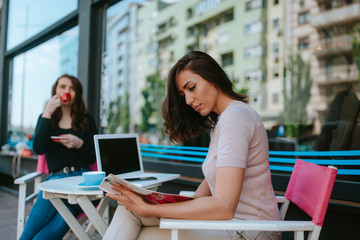 Two beautiful caucasian women are sitting in a cafe, talking and drinking coffee