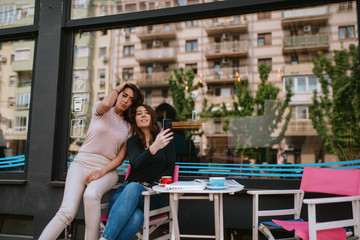Two beautiful caucasian women are sitting in a cafe and taking selfies