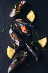 Mussels with lemon and parsley on a dark stone background, copy space. Fresh seafood