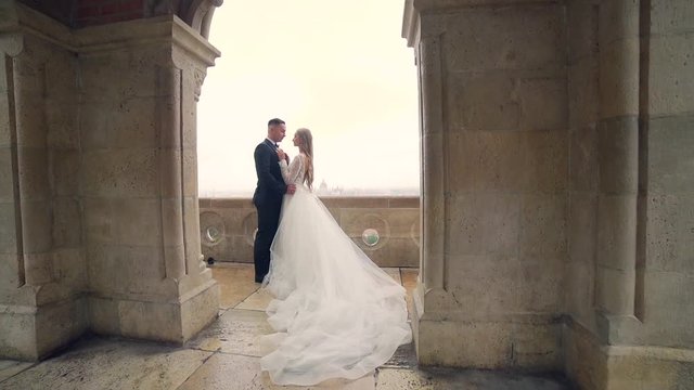 Beautiful wedding couple posing on wall castle near tower Gothic stone architecture. slow motion
bride and groom. Silhouettes on the balcony overlooking Budapest, very  the background of the old town 