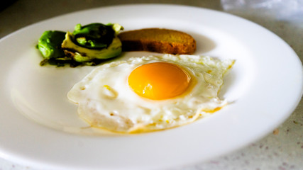 Healthy breakfast of fried eggs, bread and avocado on a white plate
