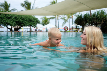 Smiling woman with child relaxing in swimming pool. Summer vacations concept