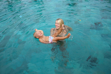 Happy infant baby boy enjoying his first swim in pool