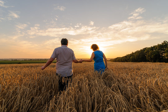 An adult farmer and his wife are walking hand in hand through their wheat field.