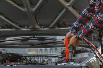 A woman holding a black and red Jumper cable that shows the positive and negative terminals to be used as a connector to stimulate the car battery to be started.Concept of car battery stimulation