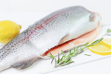 A raw trout sliced on one side with a lemon and rosemary leaves next to it. Freshwater fish.