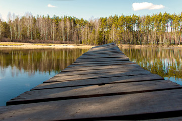wooden bridge on the lake above the water against the background of the forest