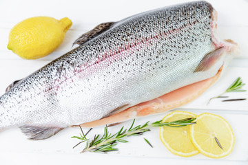 A raw decapitated trout sliced on one side with a lemon and rosemary leaves next to it. Freshwater fish.