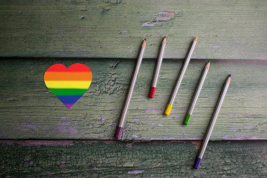 Heart painted rainbow and colorful pencils on wooden green background. LGBTQ concept