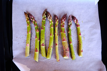 Baked asparagus on baking sheet with seasoning and olive oil