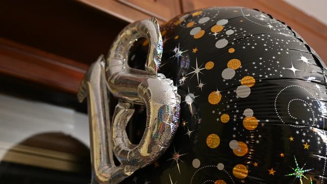 Eighteenth year birthday party: close-up image of the balloon with the number 18 made with two silver balloons covered with glitter. The ball rotates slightly. Blurry background.
