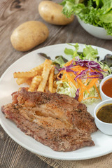 Beef steak with barbecue and paper sauces, side dish salad and french fries  served on white plate, wooden table.