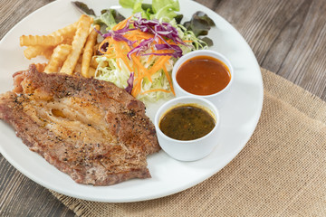Beef steak with barbecue and paper sauces, side dish salad and french fries  served on white plate, wooden table.