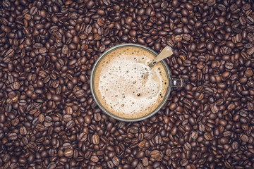 Cup of cappuccino placed in a plate of coffee beans, with Roasted Full frame coffee beans background