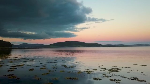 Aerial over calm water with mountains in the background and a pink sunset.