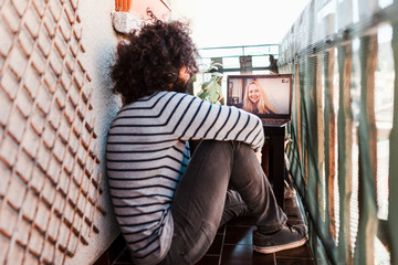 Young afro caucasian with laptop in his balcony