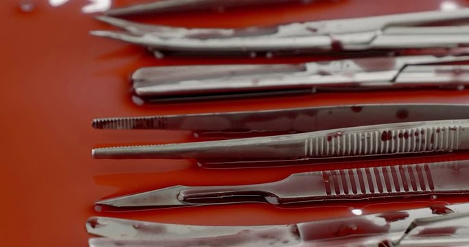 Dolly out close up of surgical instrument tools with blood, scalpel forceps tweezers, scissors for surgeon in surgery