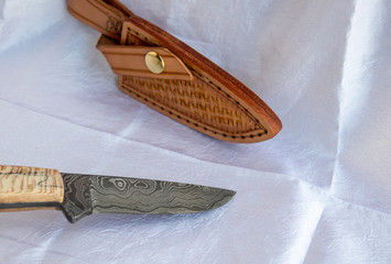 A fixed blade damascus knife and leather sheath displayed together on a white fabric. A beautiful...