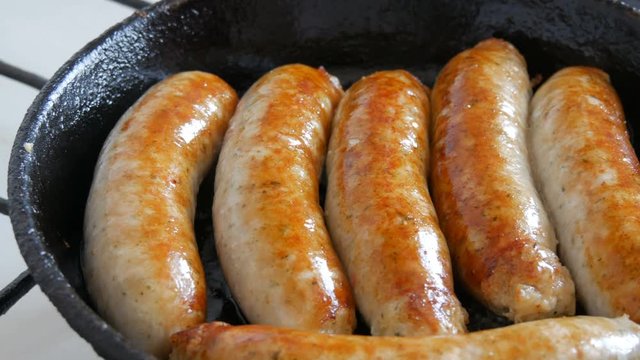 Thick fatty delicious fresh sausages are fried in a pan in the home kitchen. Fried meat products making sausages for beer. White Munich or Bavarian sausages.