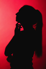 silhouette of thoughtful girl on red lightened background, unrecognizable woman profile with long hair ponytail, concept female beauty, seduction