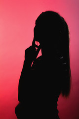 silhouette of thoughtful girl on red lightened background, unrecognizable woman profile with long hair ponytail, concept female beauty, seduction