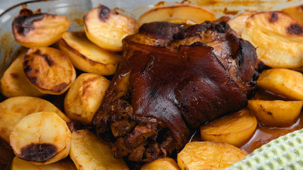Roast pork knuckle in the oven. Meat and fried potatoes. Homemade food. Glass dish for the oven. Fork and knife.