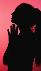 silhouette of thoughtful girl with head up on red lightened background, unrecognizable woman face profile, concept emotions, stress, religion