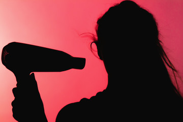 silhouette of a beautiful woman profile doing a hairstyle with hair dryer on red background, concept of beauty and danger