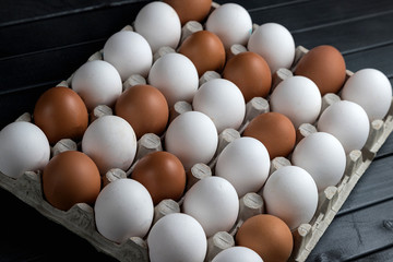 white and brown chicken eggs in one clutch. Village product. Eggs on a dark wooden table.