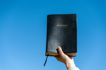 Raised hand holding the Holy Bible. Background with blue sky on a beautiful winter morning. Copy...