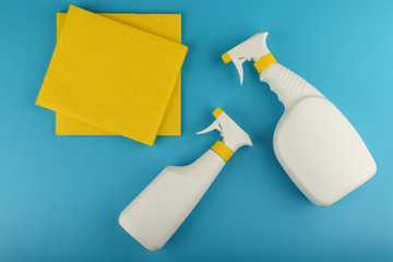 white spray bottles detergent or sanitizer and yellow cleaning cloth on blue background flat lay with mock up