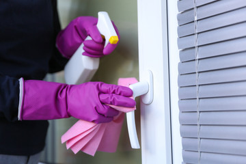 cleaner's hands in rubber gloves doing disinfection cleaning door handle with detergent spray and...