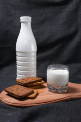 Cookies on a wooden cutting board. A glass of milk and a bottle of milk. Milk products. Photo of food on a dark background.