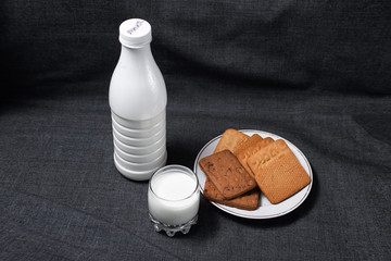 Cookies on a wooden cutting board. A glass of milk and a bottle of milk. Milk products. Photo of food on a dark background.