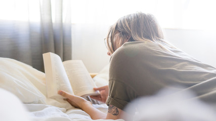 Woman engrossed reading a book at home on the bed in the daytime