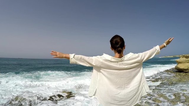 Woman standing on coast in Malta facing sea waves stretching arms and feeling strong breeze. Holidays concept, traveling concept.