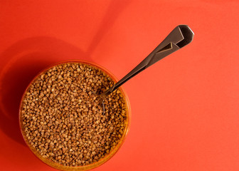 raw buckwheat in a plastic container with a spoon on a red background