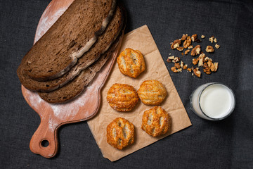 Baking, rolls, bread and milk on a dark background. Kraft, food paper and wooden board