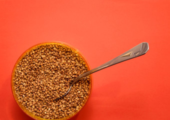 raw buckwheat in a plastic container with a stuck spoon on a red background