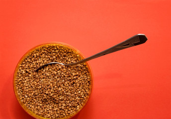 raw buckwheat in a plastic container with a stuck spoon on a red background