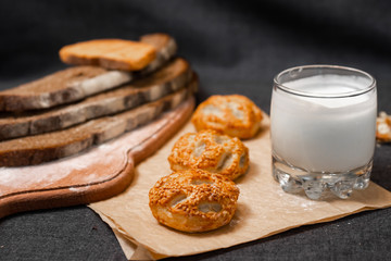 Baking, dark bread, cookies and rolls on a dark background.
Kraft paper. Milk in a transparent glass.