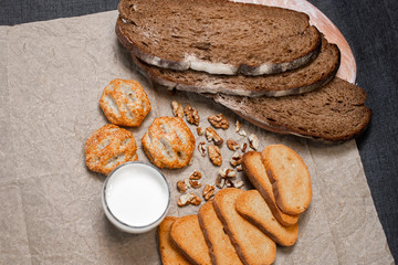Baking, dark bread, cookies and rolls on a dark background.
Kraft paper. Milk in a transparent glass.