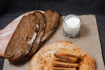 Baking, dark bread, cookies and rolls on a dark background.
Kraft paper. Milk in a transparent glass.