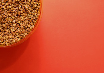 uncooked buckwheat in a container on a red background in the corner