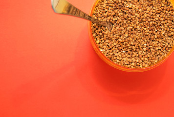 uncooked buckwheat in a container with a spoon on a red background