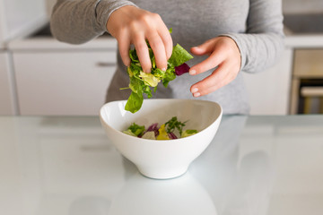 Green leaf salad in the white bowl on kitchen table. Woman. Salad preparation. Healthy lifestyle and nutrition concept.