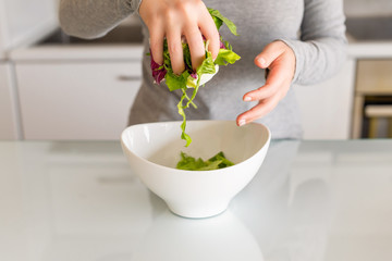 Green leaf salad in the white bowl on kitchen table. Woman. Salad preparation. Healthy lifestyle and nutrition concept.