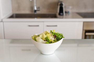 Green leaf salad in the white bowl on kitchen table. Salad preparation. Healthy lifestyle and nutrition concept.