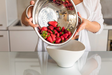 Clean red ripe strawberries in a stainless steel colander are rinsed under water in a woman hand